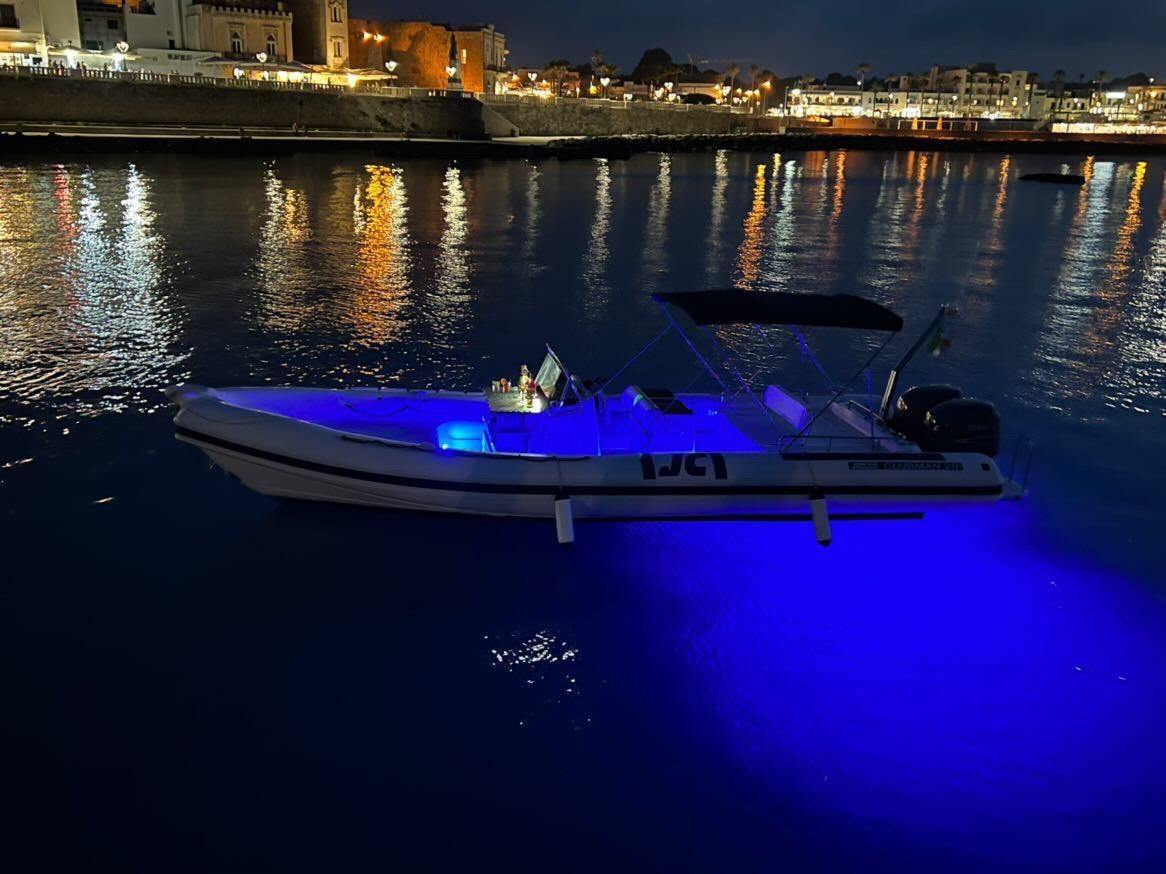 Gommone di Alfiere Escursioni di notte ad Otranto illuminato, con la città in secondo piano