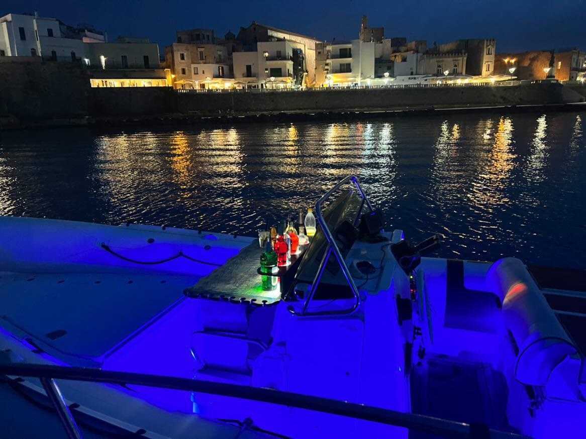 Un dettaglio del gommone con le luci della costa idruntina in secondo piano di notte